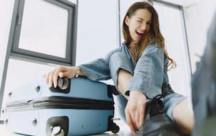 TravelSecure: Vor der Reise Gut vorbereitet sein (junge fröhliche Frau mit gepacktem Koffer)